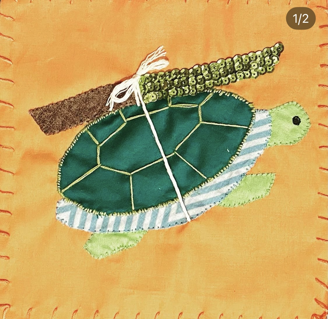 A hand embroidered flag of a stabby turtle, green shell with a green sequins utility knife tied on top.