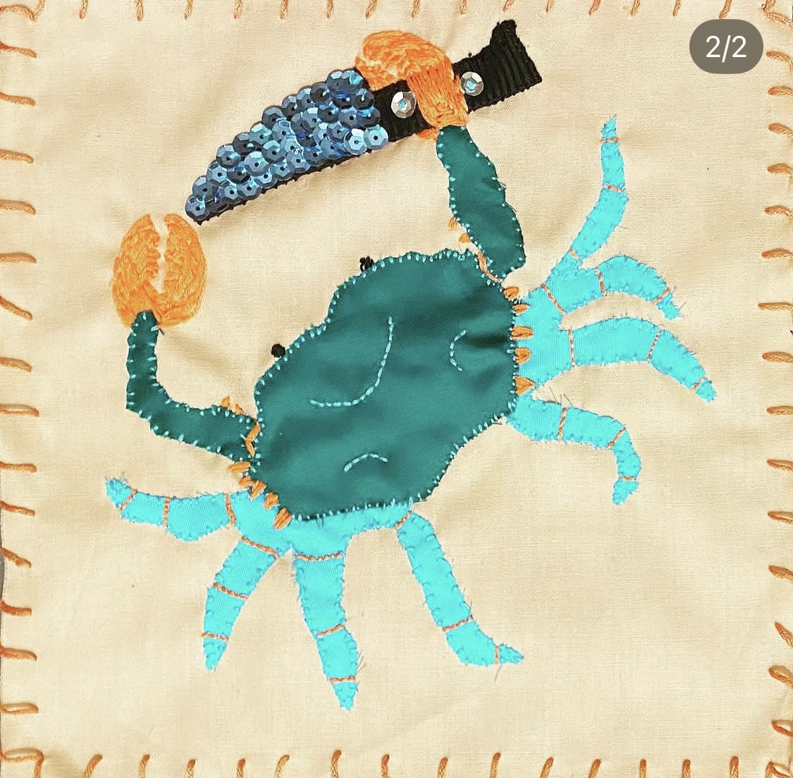 A hand embroidered pirate flag of a stabby crabby. A blue and teal crab with a blue sequins paring knife in its right claw.